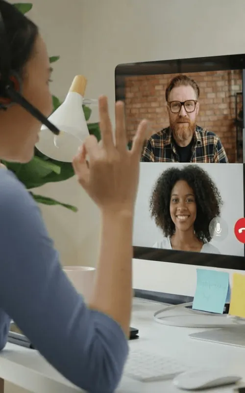 Worker at a desk greeting two colleagues on a desktop video call